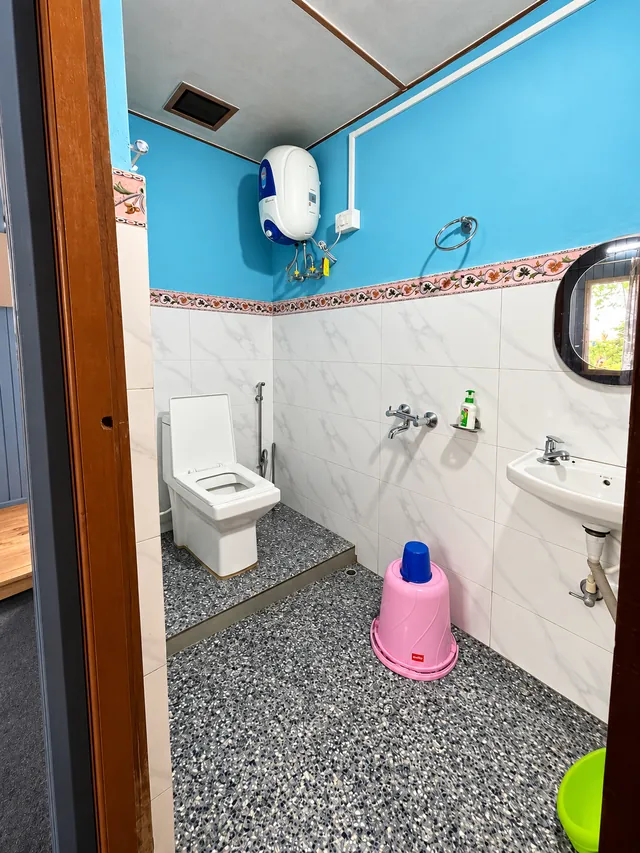 A tiled bathroom with blue upper walls, a wall-mounted sink, shower fittings, and a water heater