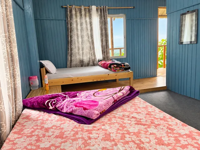 A double bed and a single bed beside curtained windows in a blue-panelled room