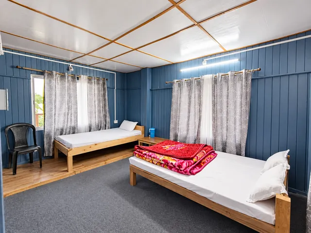 Two wooden beds with white linen and folded red blankets in a blue-panelled guest room