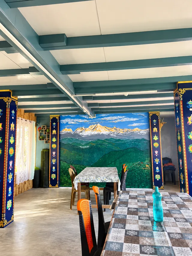A long dining table, painted pillars, and a mountain mural in the shared dining hall