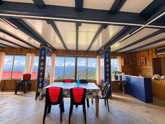 A shared dining area with red chairs, wooden ceiling beams, and windows facing the mountains
