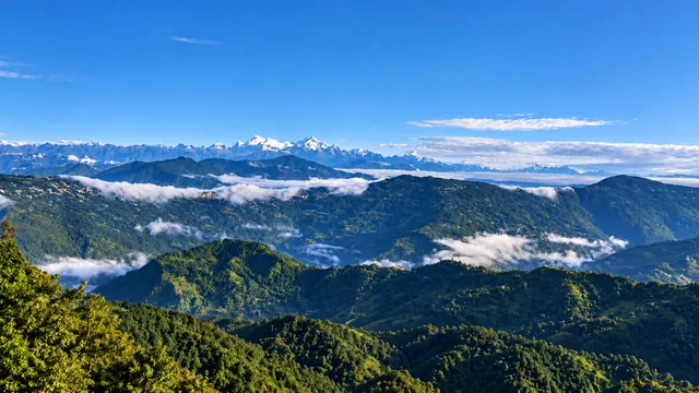 A wide view of green hills, drifting clouds, and a snowy mountain range beneath a blue sky
